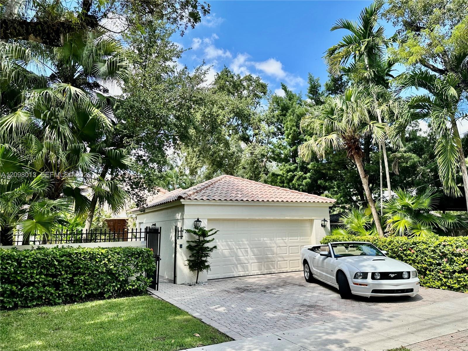 garage featuring a tile roof, stucco exterior, paver driveway, and black metal perimeter fencing surrounded by mature landscaping