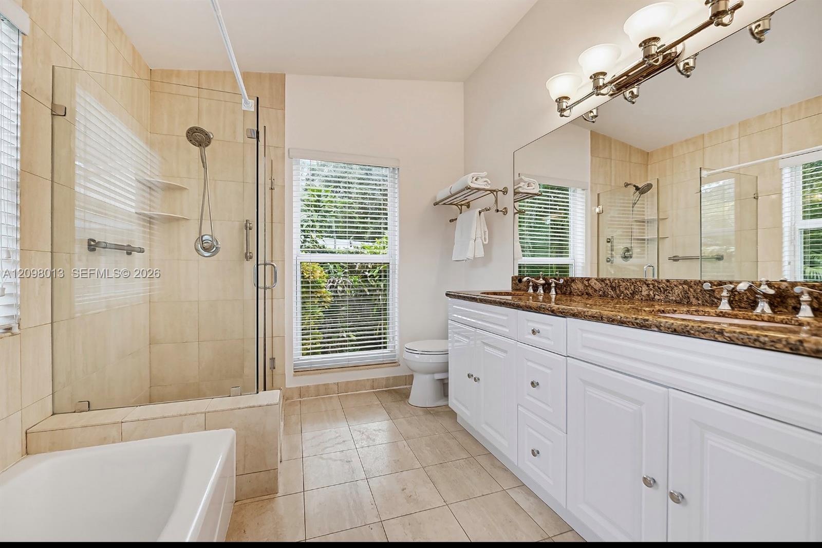 Bathroom featuring a double-sink vanity with stone countertop, walk-in glass-enclosed shower, separate tub tub