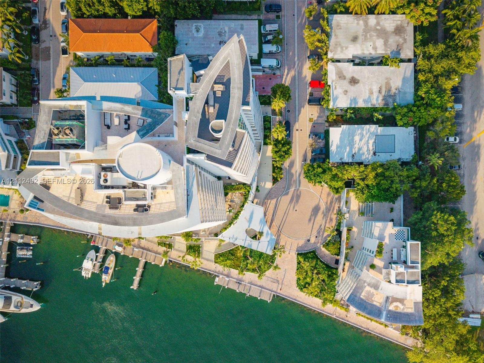 Aerial perspective of a multi-level waterfront estate featuring a private deep-water dock, extensive rooftop terrace space, and hardscaped circular mo