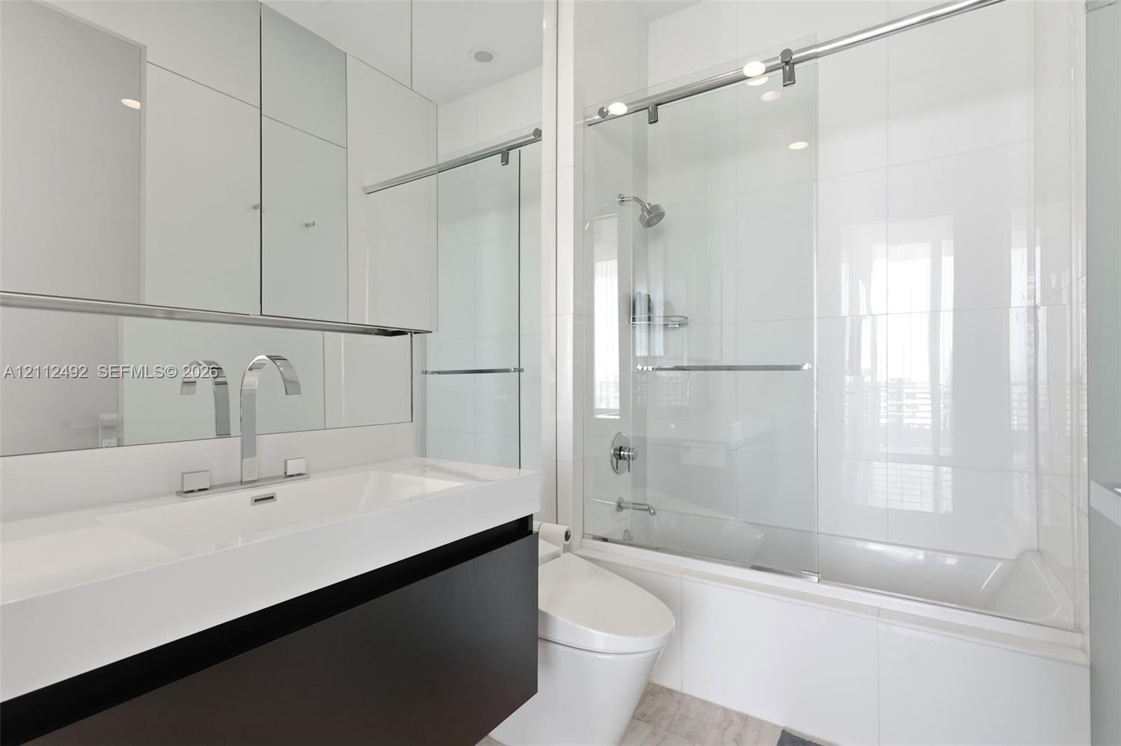 Modern vanity with integrated rectangular basin and polished chrome widespread faucet, mirrored medicine cabinet, floor-to-ceiling tiled shower enclos