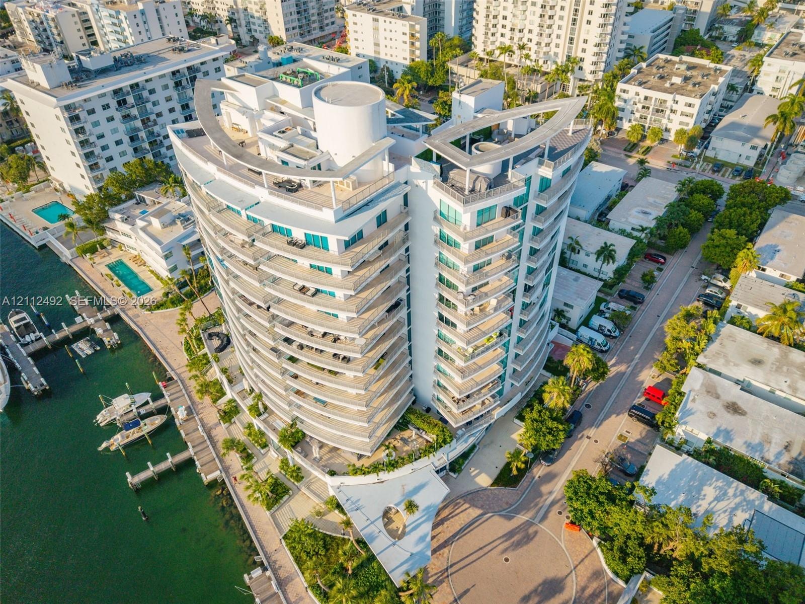High-rise multi-story building featuring curvilinear architectural design, extensive glass-paneled balconies, a rooftop terrace, and a private dock fa