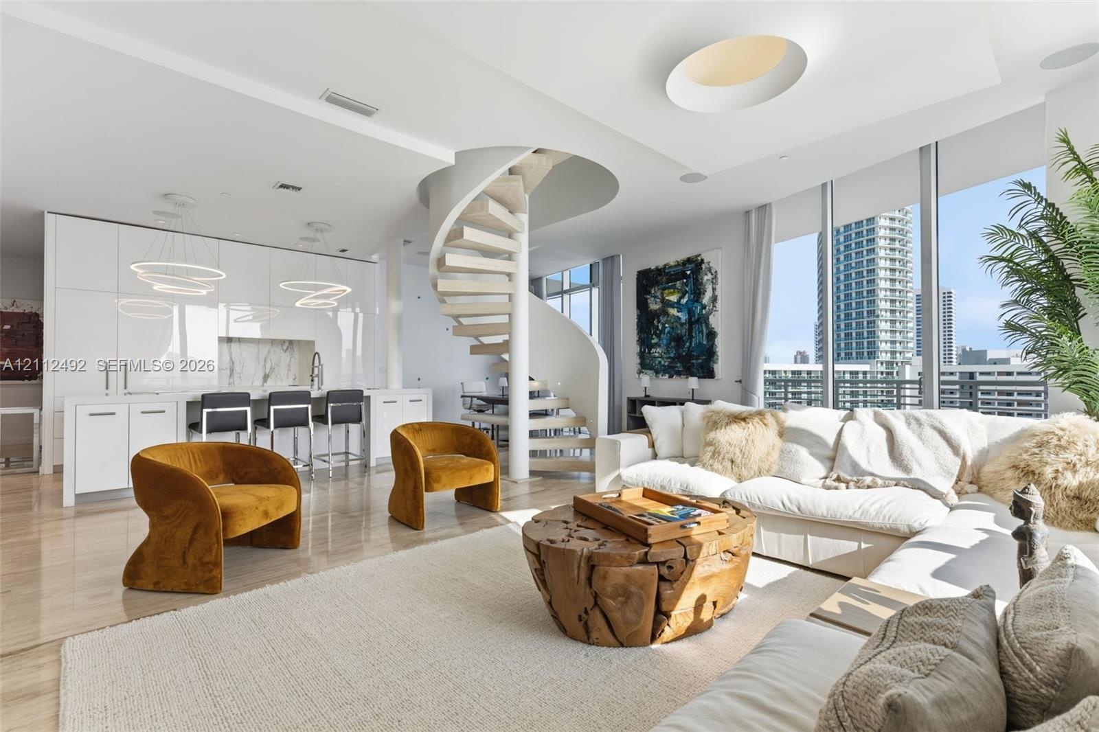 Open-concept living space featuring a sculptural spiral staircase, high-gloss flat-panel cabinetry, floor-to-ceiling windows, and polished stone floor