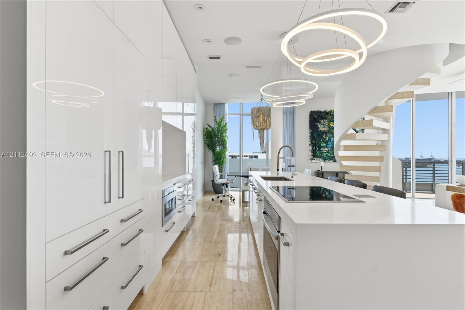 High-gloss cabinetry, stone-surfaced kitchen island, integrated stainless steel appliances, circular pendant lighting, and a sculptural spiral stairca