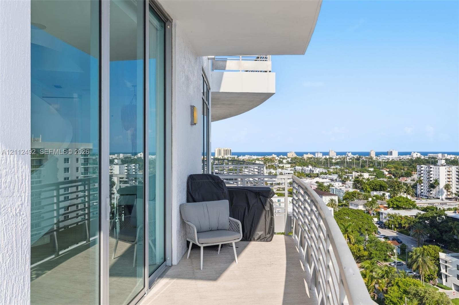 Covered balcony featuring full-height glass sliding doors, concrete flooring, and metal railings with coastal city scenery