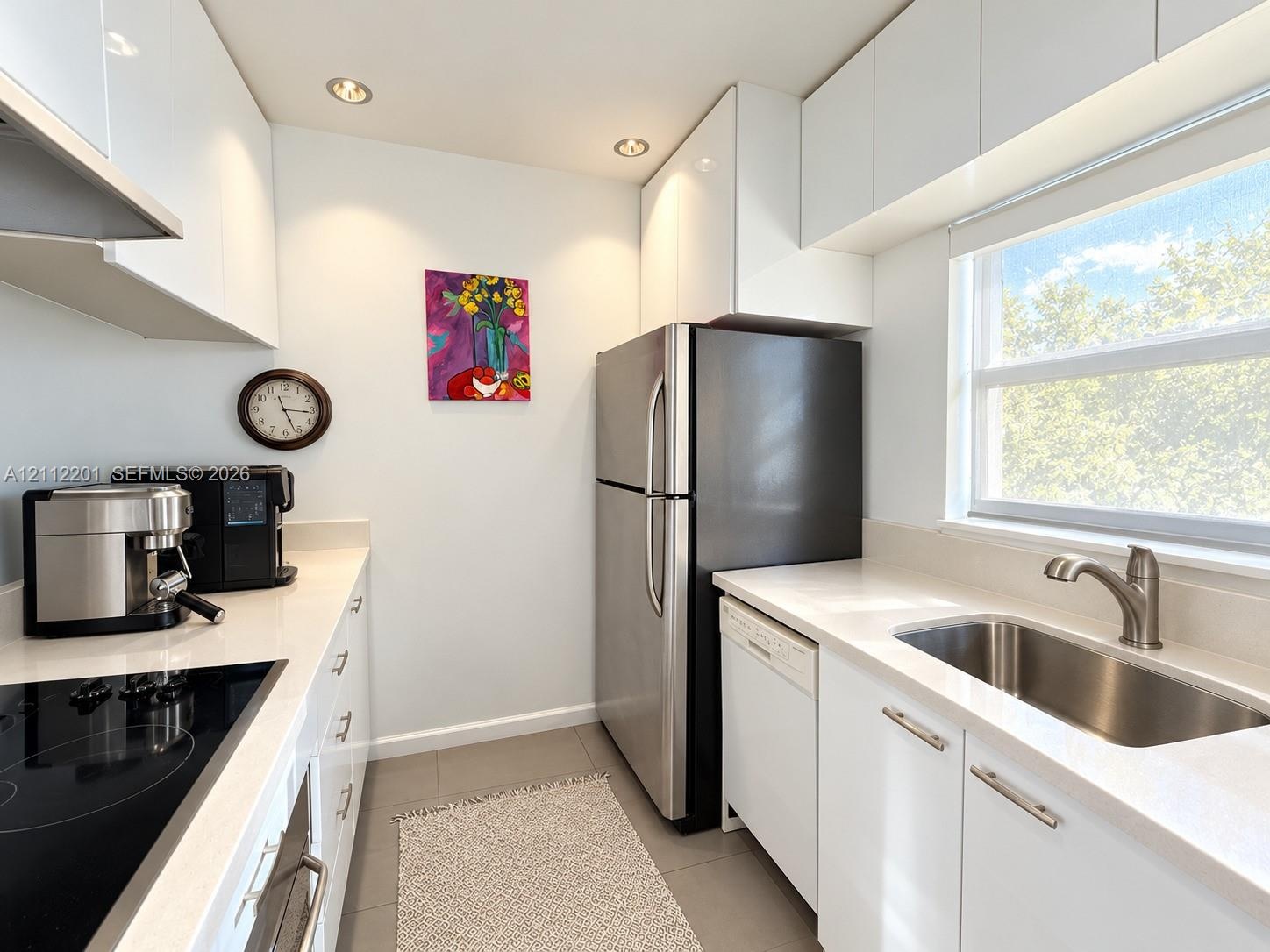 Kitchen featuring white flat-panel cabinetry, light-toned solid surface countertops, stainless steel refrigerator, undermount sink with gooseneck fauc