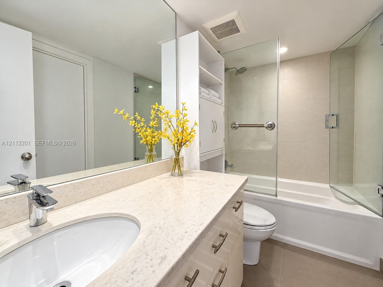 Bathroom featuring a solid-surface countertop with an integrated basin, high-gloss cabinetry, built-in shelving, a full-width vanity mirror, and a til