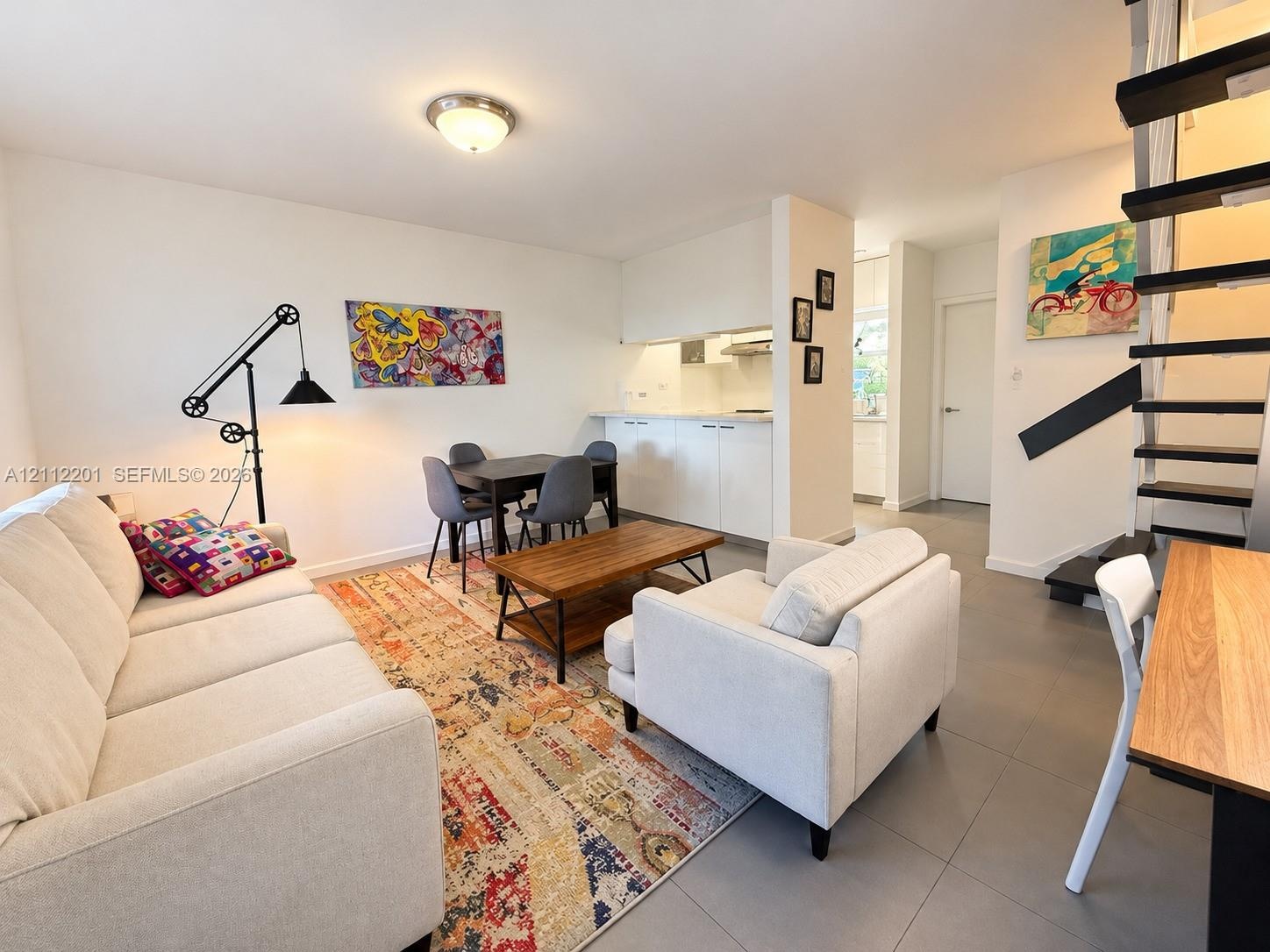 Open-concept living space featuring large-format tile flooring, sleek minimalist cabinetry, and a black metal staircase with open treads