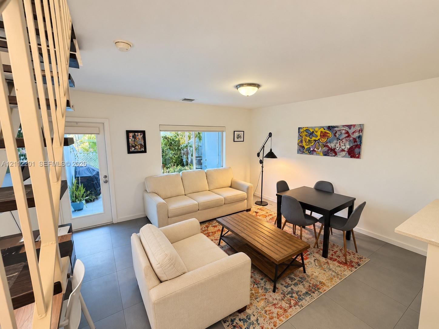 Open-concept interior featuring large-format tile flooring, metal open-tread staircase, and a glass-paneled exterior door