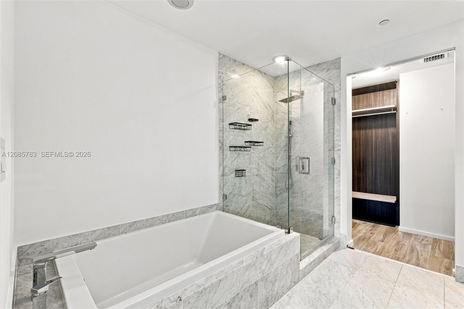 Soaking tub featuring stone-finish surround, glass-enclosed shower with rainfall showerhead, and built-in closet cabinetry