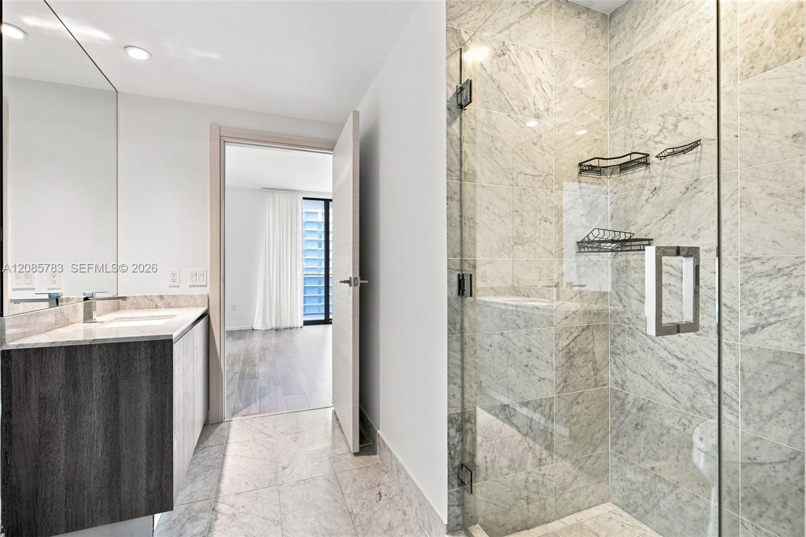 Bathroom featuring stone-finish flooring, glass-enclosed shower with full-height stone-finish wall tile, and vanity with stone-finish countertop