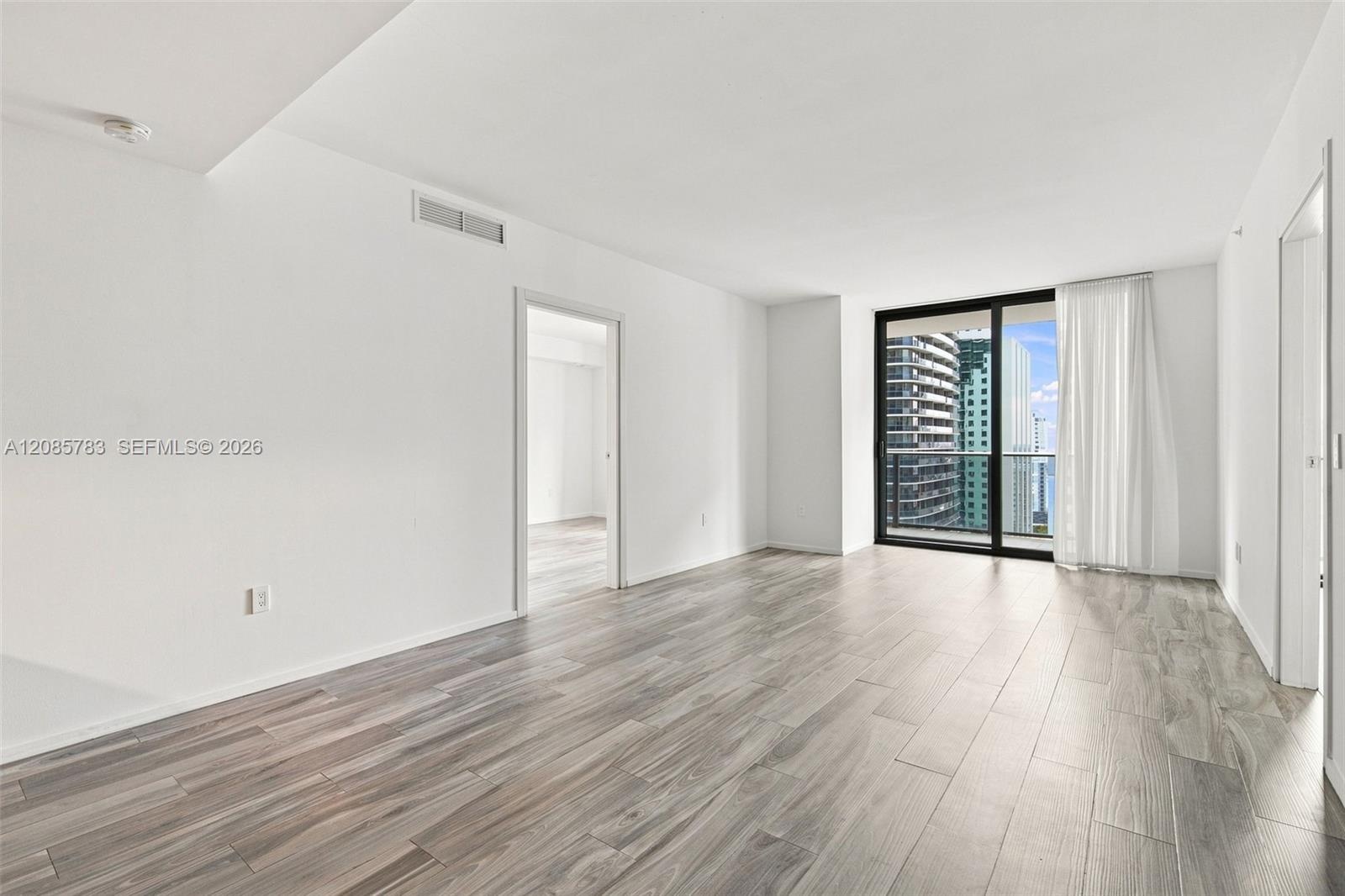 Open floor plan featuring wood-finish flooring, floor-to-ceiling glass sliding doors, and access to a balcony