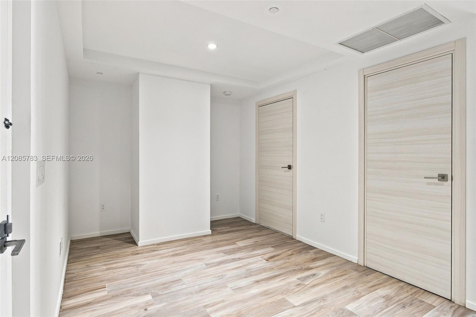 Interior space featuring tray ceiling, wood-finish flooring, and two interior doors with horizontal grain finish