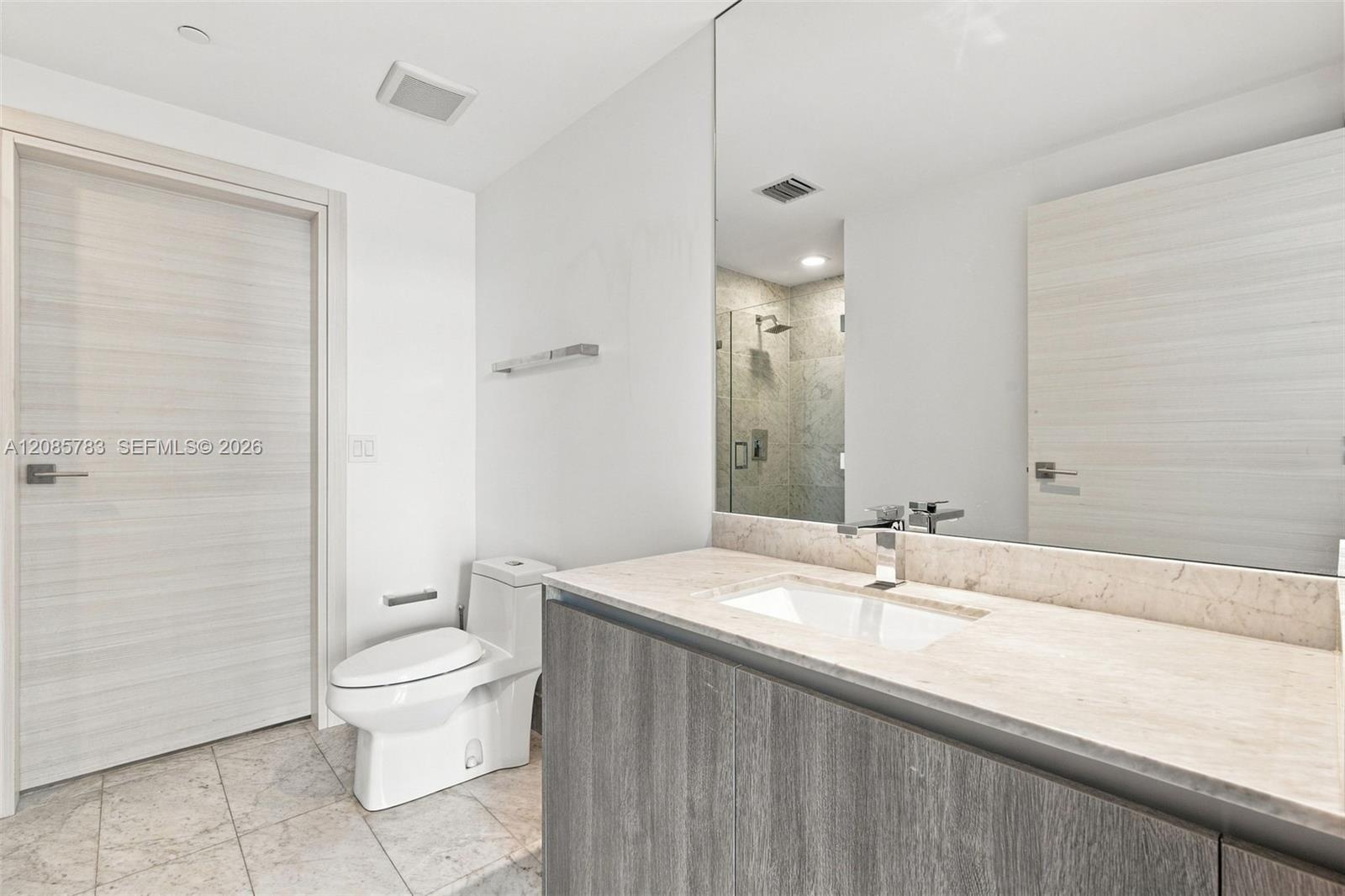 Bathroom featuring a vanity with stone countertop and integrated sink, full-width wall mirror, wood-finish cabinetry, two-piece toilet, and tile floor