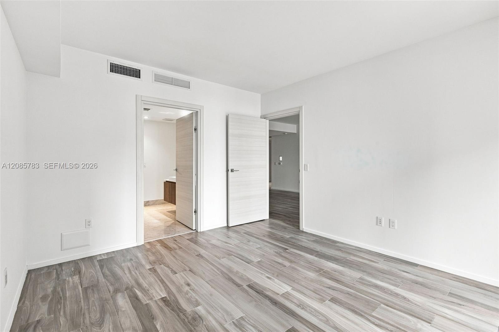 Interior room featuring neutral wall finishes, wood-finish flooring, and light-tone wood grain doors with metallic hardware