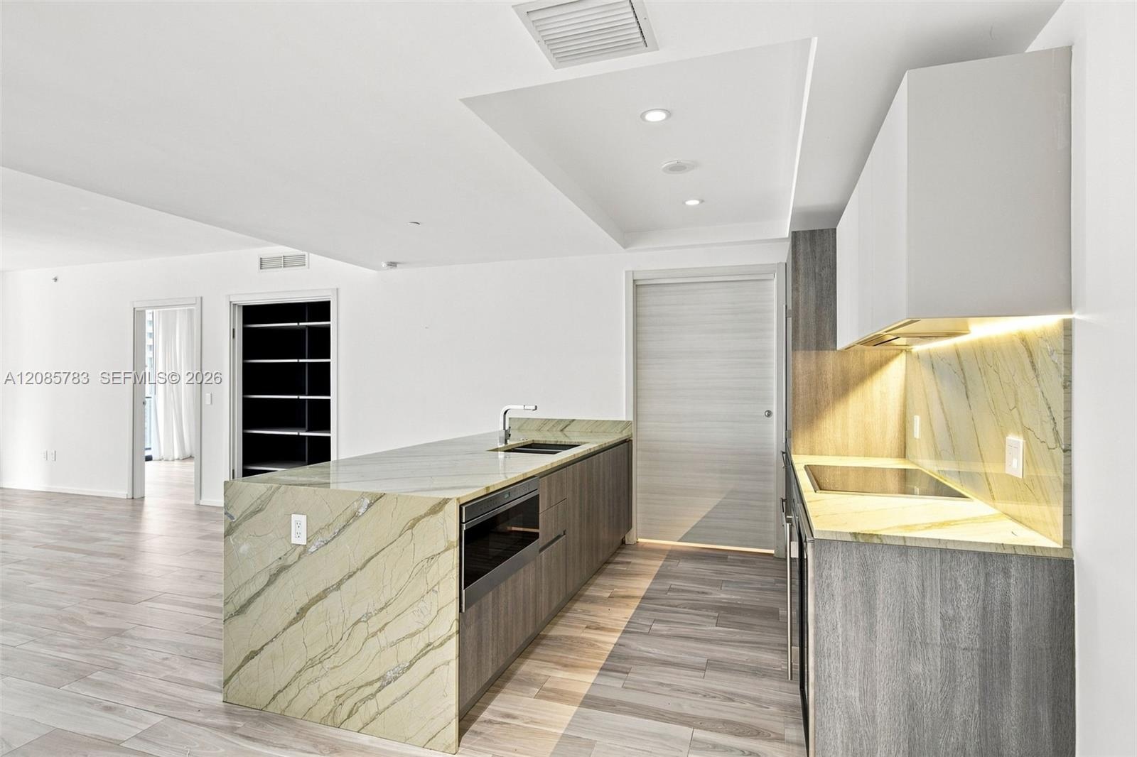 Kitchen featuring flat-panel cabinetry, stone countertops with matching full-height backsplash, waterfall-edge island with an integrated microwave, an