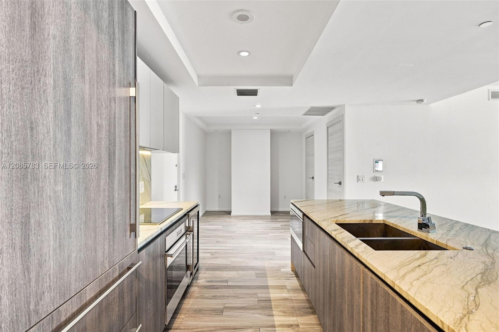 Kitchen featuring wood-finish cabinetry, natural stone countertops, a double-basin undermount sink with a gooseneck faucet, integrated stainless steel