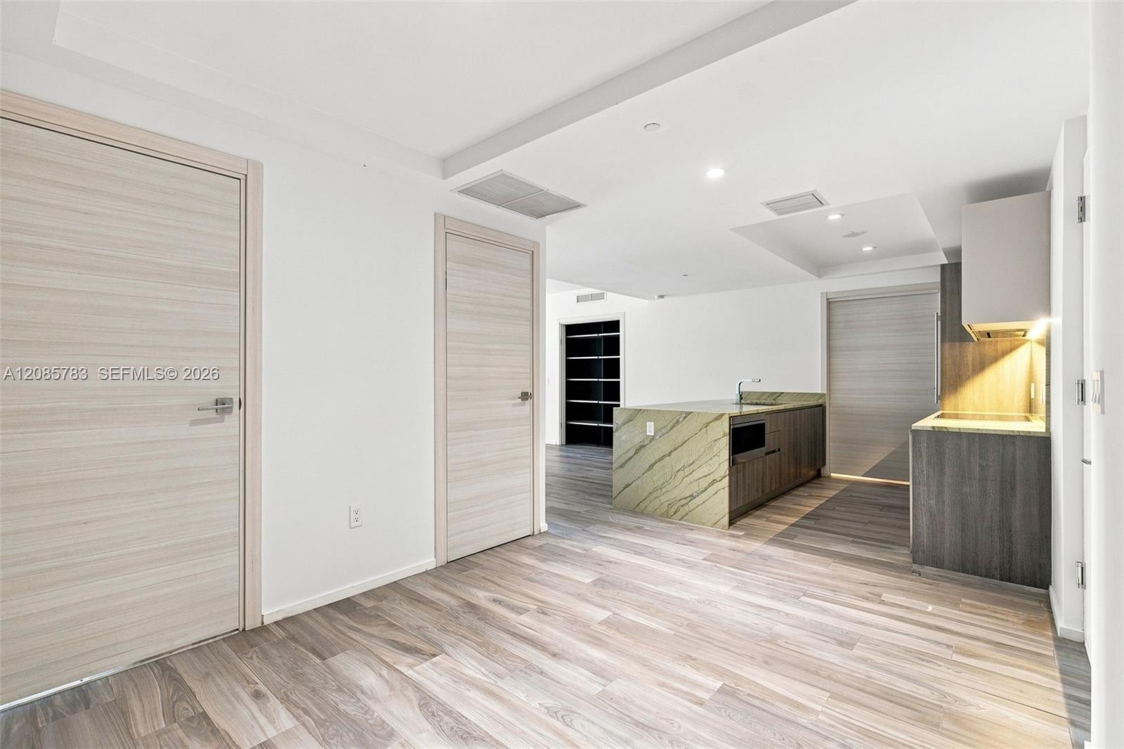 Kitchen featuring a stone-topped island, wood-finish flooring, built-in cabinetry with integrated under-cabinet lighting, and flat-panel interior door