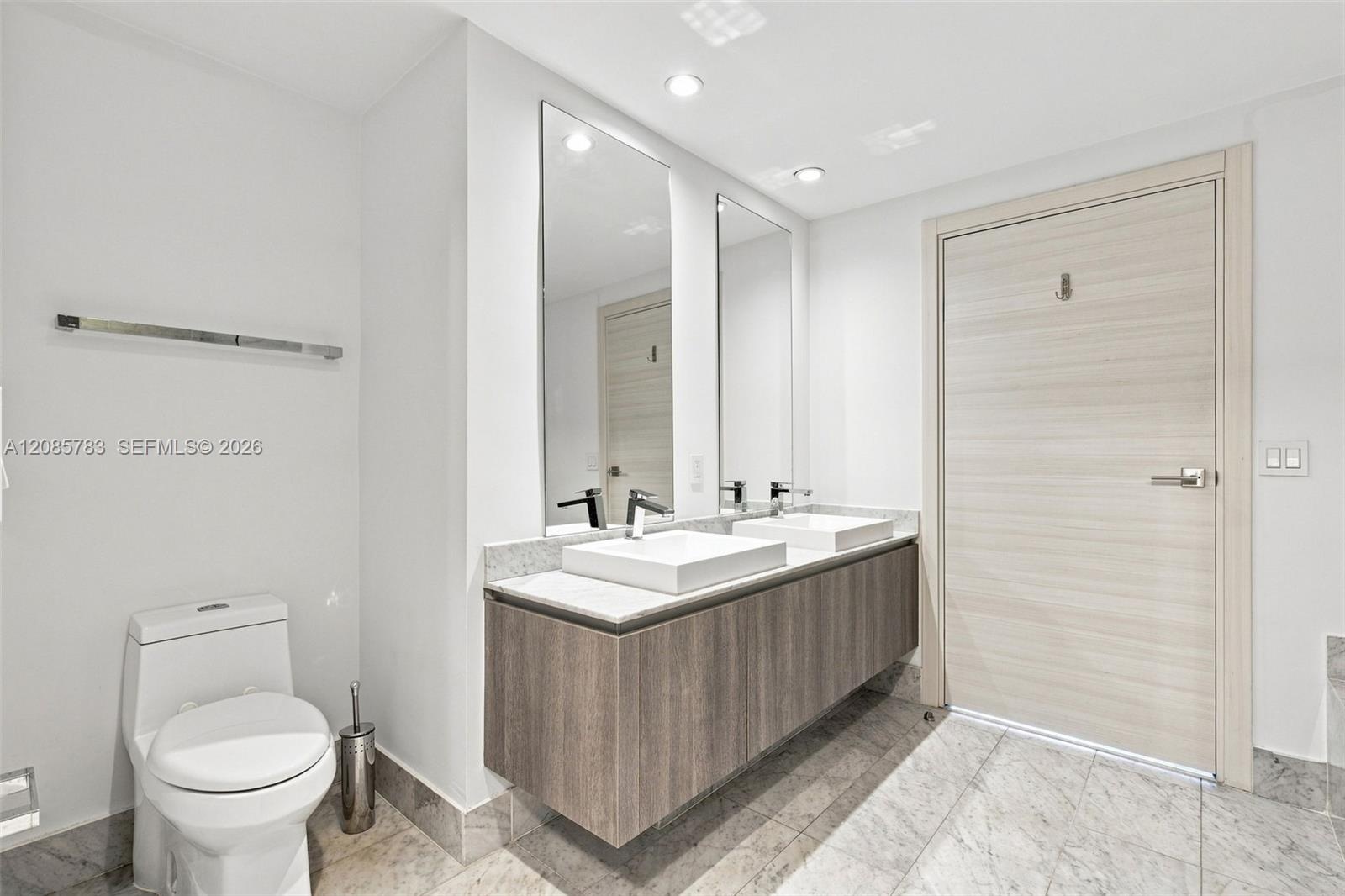 Floating vanity with dual rectangular vessel sinks, stone-surface countertop, full-height wall mirrors, and wood-finish door