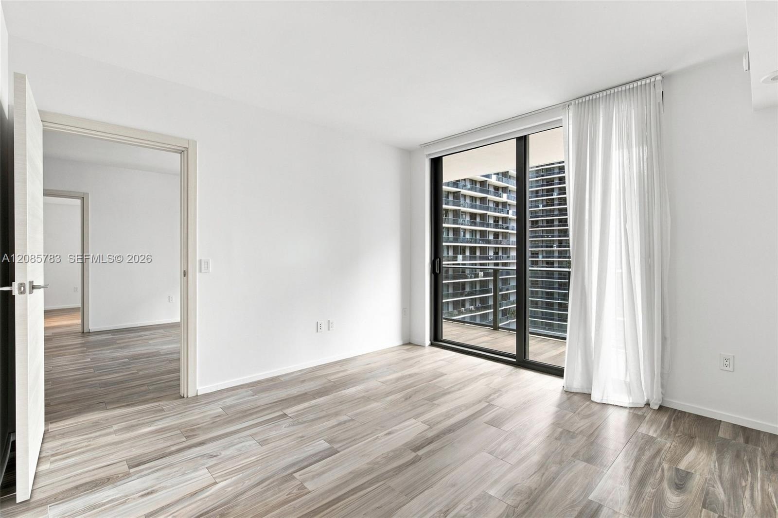 Wood-finish flooring, full-height sliding glass doors, private balcony, and neutral wall finishes