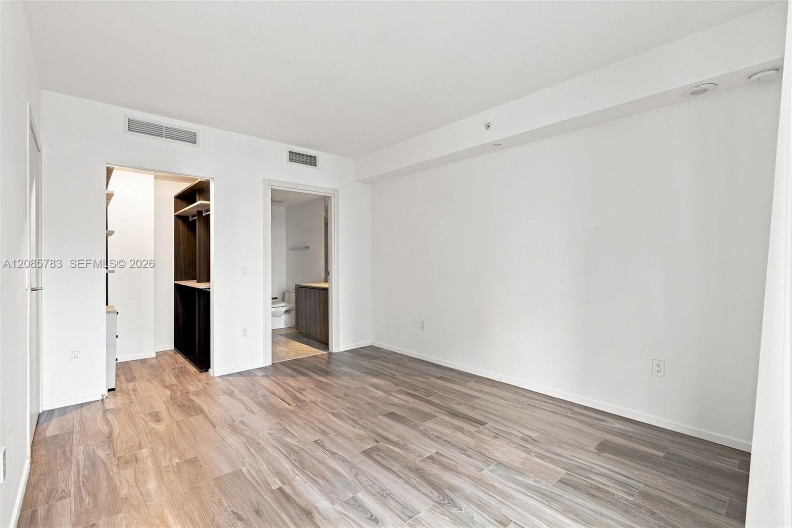 Room featuring wood-finish flooring, built-in closet cabinetry with shelving, and an integrated bathroom vanity