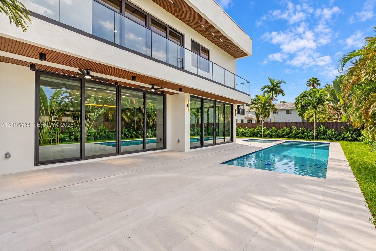 Modern exterior featuring a wrap-around glass balcony, oversized floor-to-ceiling sliding glass doors, a stone-tiled patio, and an in-ground swimming 