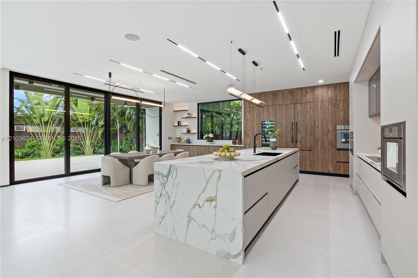 Kitchen featuring an oversized island with stone-finish waterfall countertop, wood-finish cabinetry, floor-to-ceiling glass sliding doors, integrated 