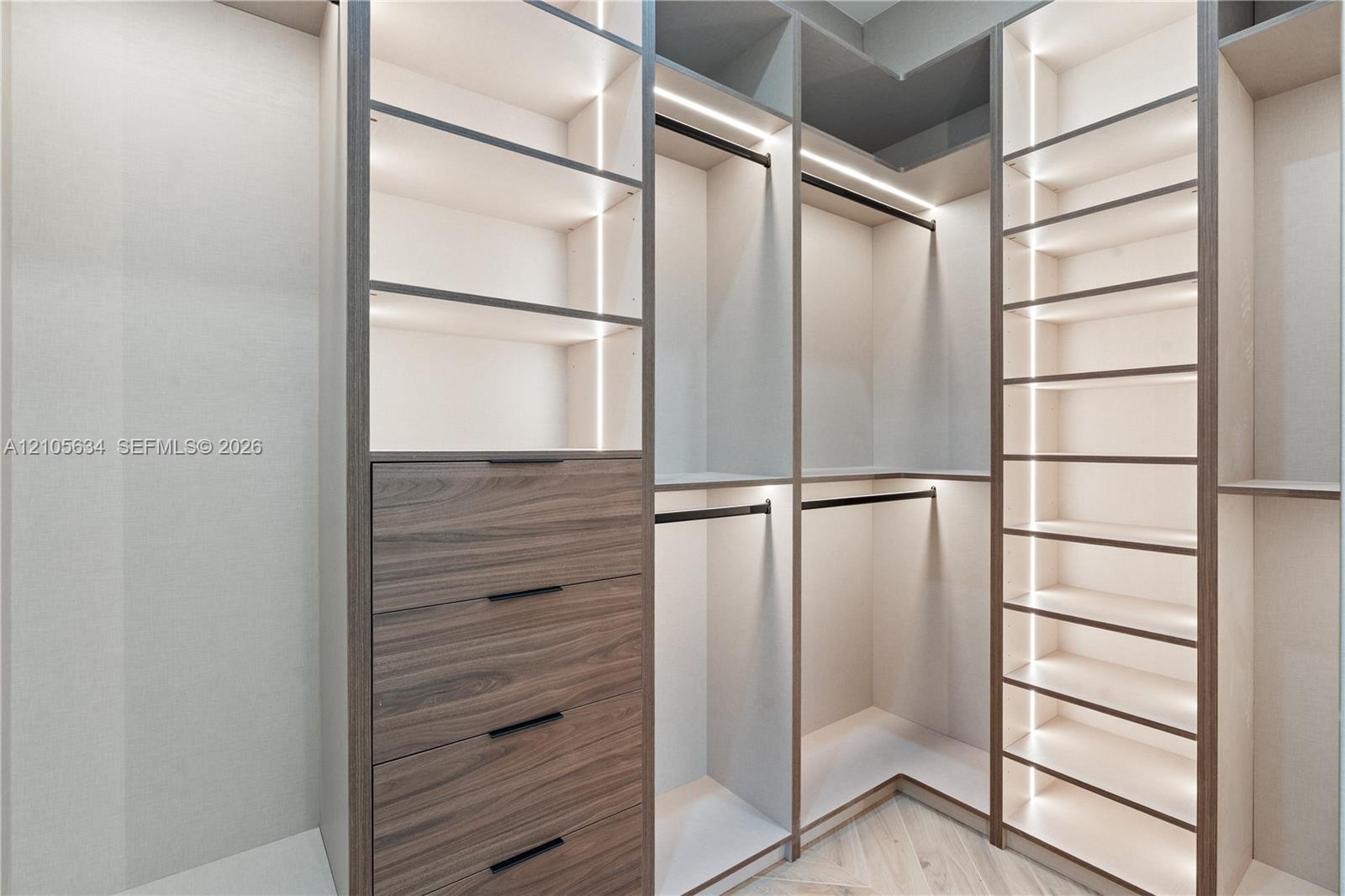 Custom floor-to-ceiling built-in cabinetry featuring wood-finish drawer fronts, integrated linear vertical lighting, adjustable open shelving, and mat