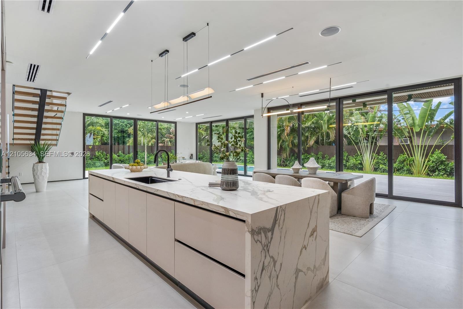 Kitchen featuring a large central island with waterfall-edge stone countertops, custom flat-panel cabinetry, matte black hardware, floor-to-ceiling mu