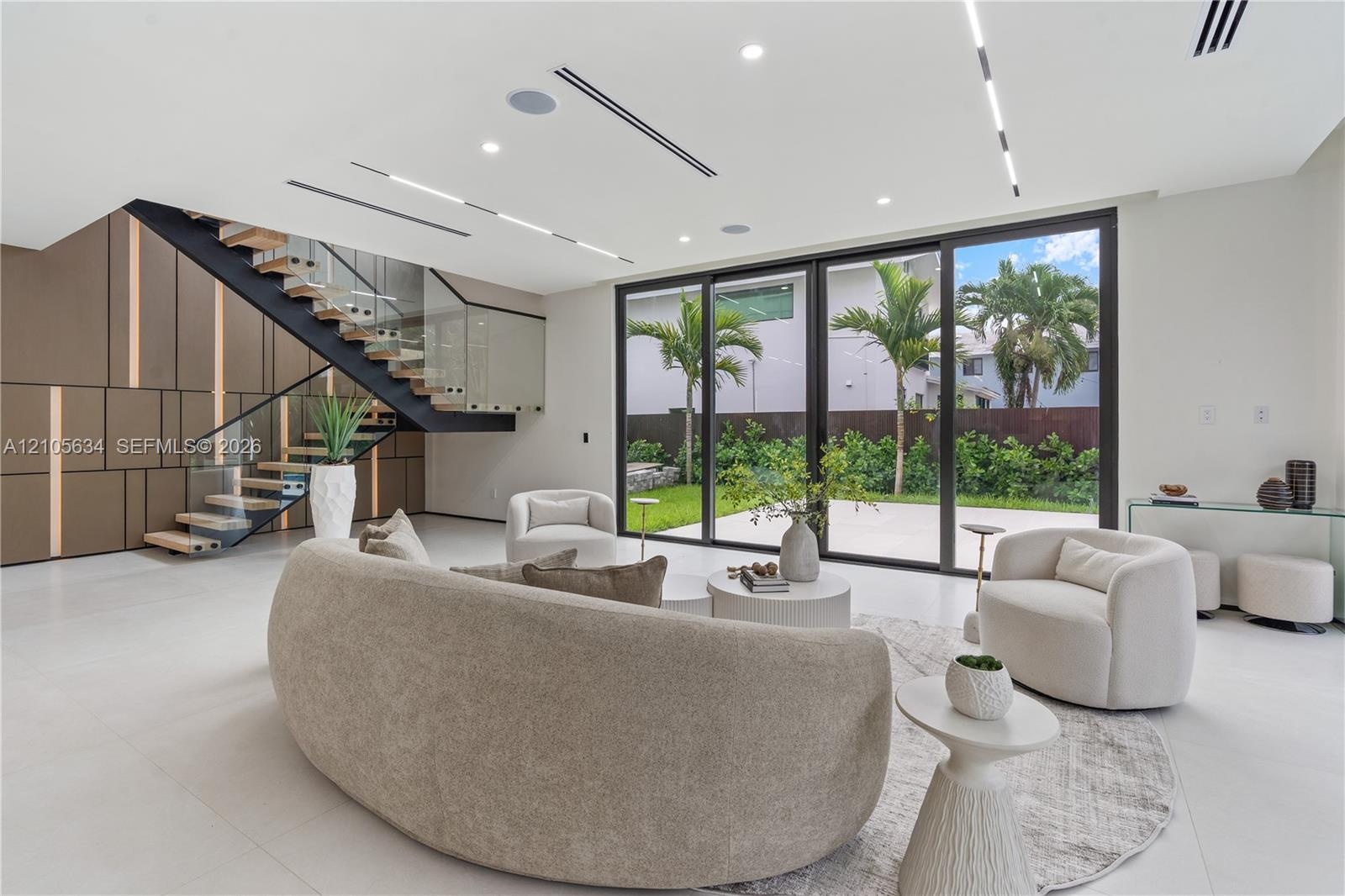 Open-concept interior featuring large-format tile flooring, a custom metal staircase with a glass railing, built-in decorative wall paneling, and floo