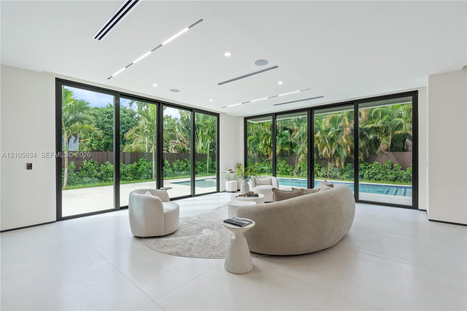 Large-format sliding glass doors, polished porcelain flooring, recessed linear lighting, built-in ceiling speakers, and perimeter patio access