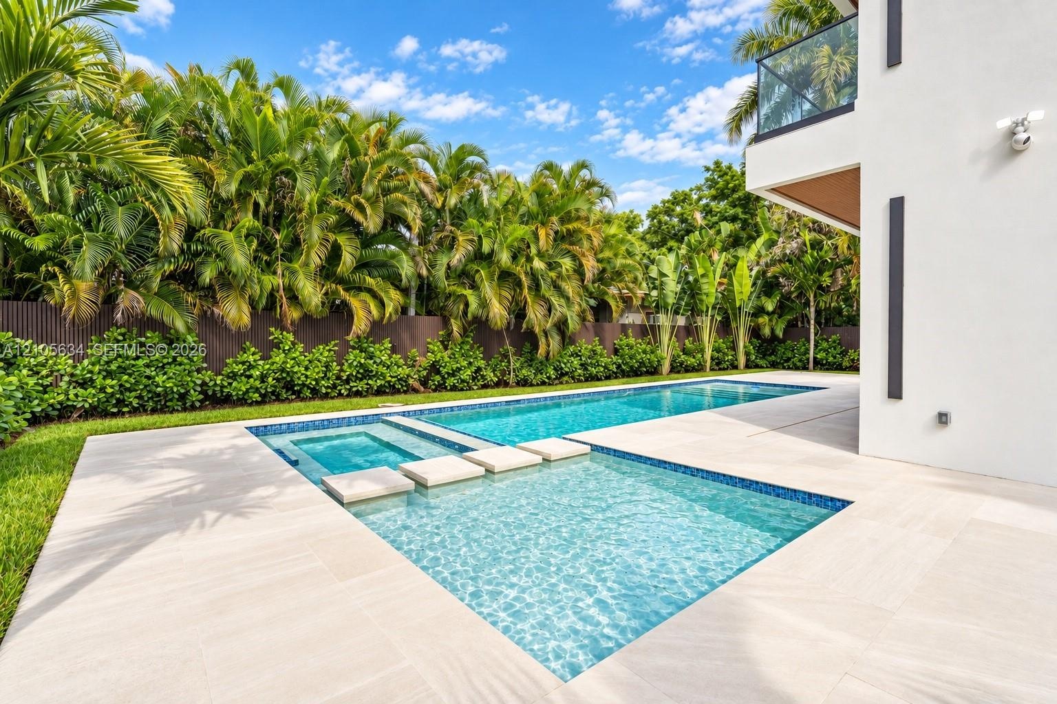 In-ground swimming pool with an integrated spa, featuring stone-style paver decking, decorative concrete stepping stones, and surrounding lush landsca