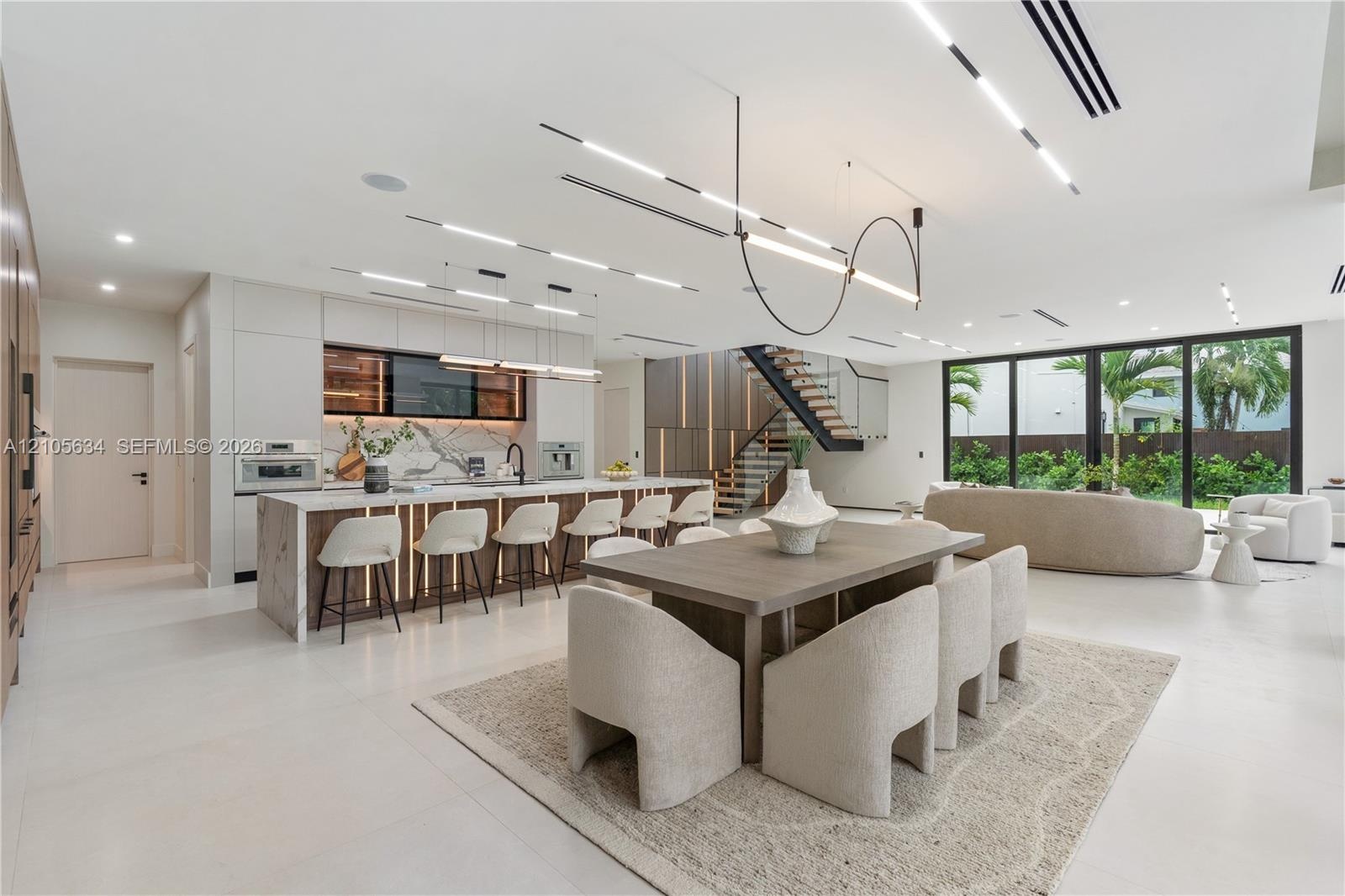 Open-concept interior featuring large-format flooring, a kitchen island with stone-surface counters, integrated LED accent lighting, floating staircas
