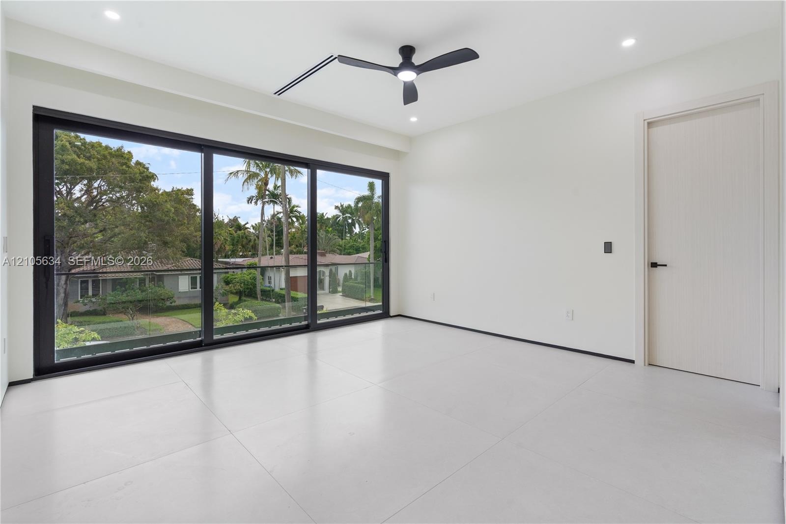 Floor-to-ceiling sliding glass doors with black frames, large-format tile flooring, recessed lighting, matte black ceiling fan, and solid-core interio