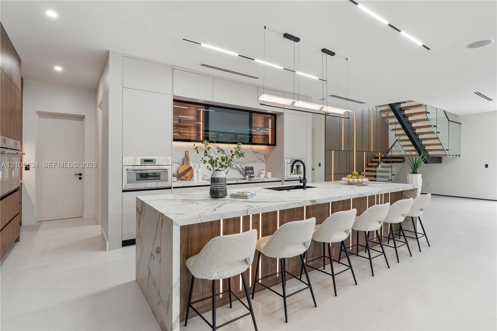 Modern kitchen featuring a waterfall-edge island with stone-finish surfaces and integrated wood-paneling, flat-panel cabinetry, built-in stainless ste