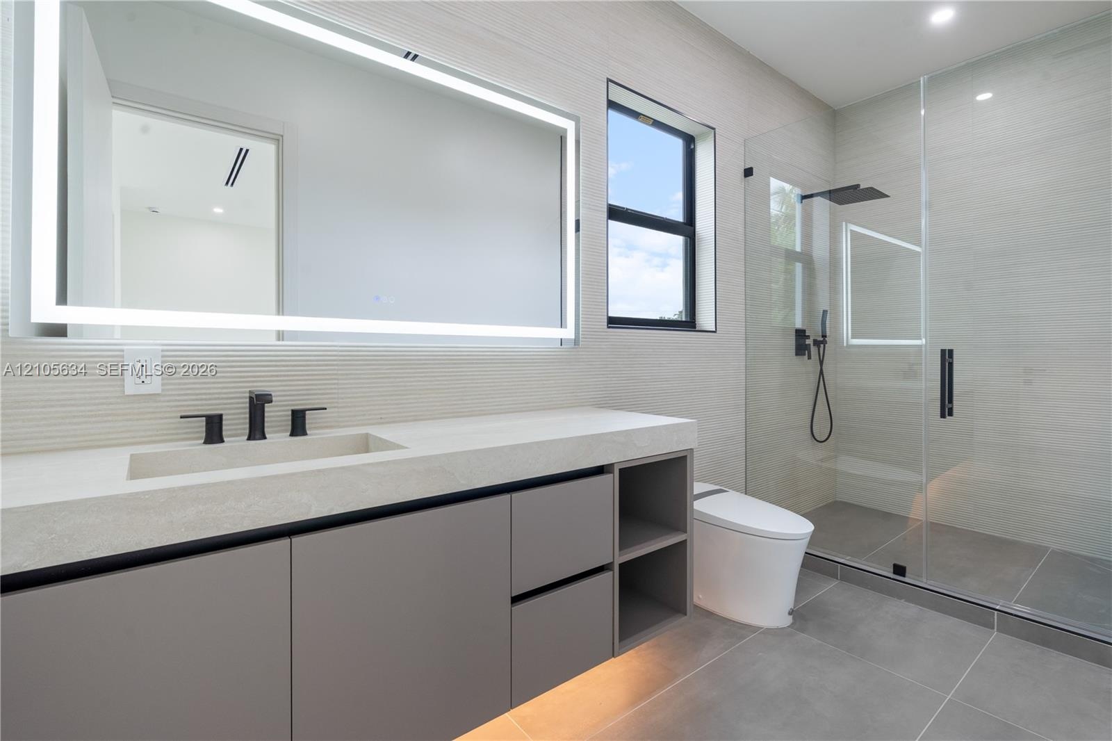 Floating vanity with integrated sink, stone-finish countertop, under-cabinet lighting, LED-backlit mirror, and glass-enclosed walk-in shower with matt