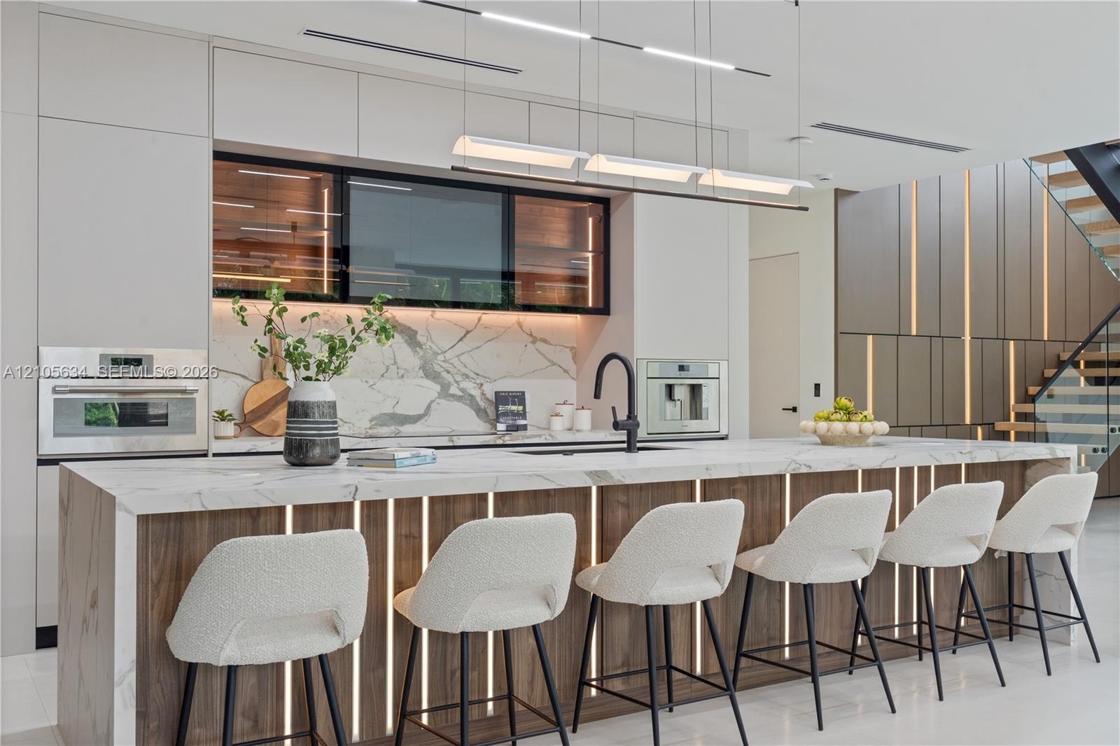 Contemporary kitchen featuring a stone-surface waterfall island with integrated vertical lighting, flat-panel cabinetry, a stone backsplash, built-in 