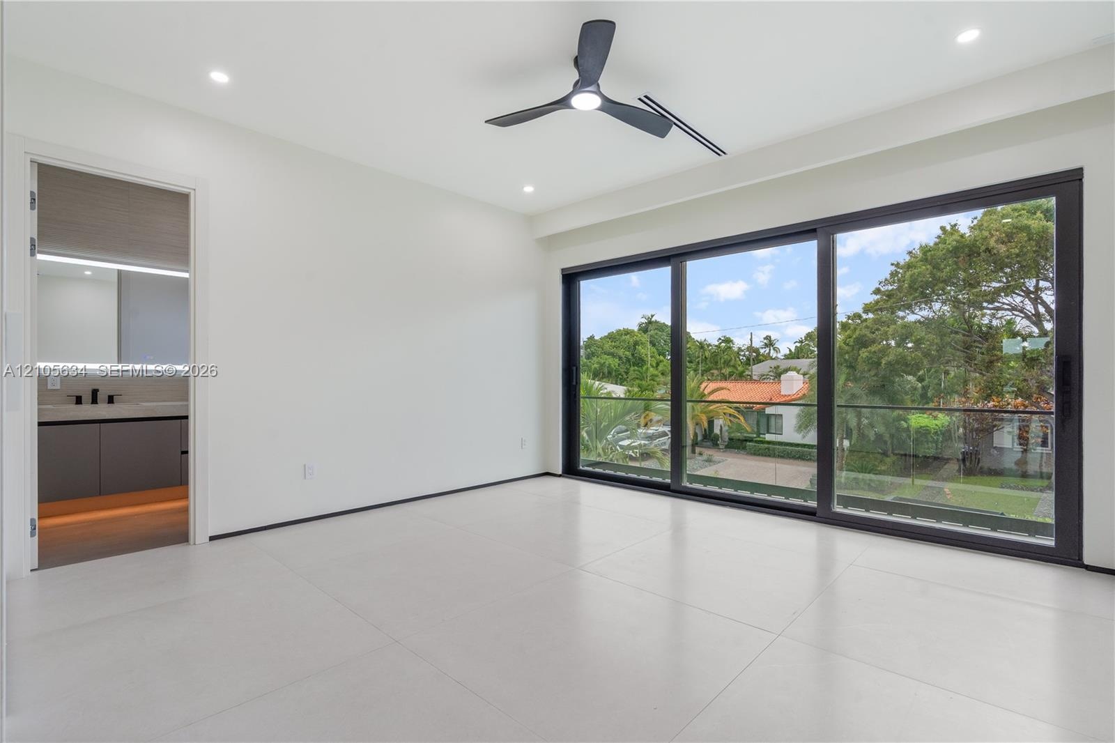 Large-format porcelain tile flooring, expansive floor-to-ceiling sliding glass doors with black frames, recessed LED lighting, three-blade ceiling fan