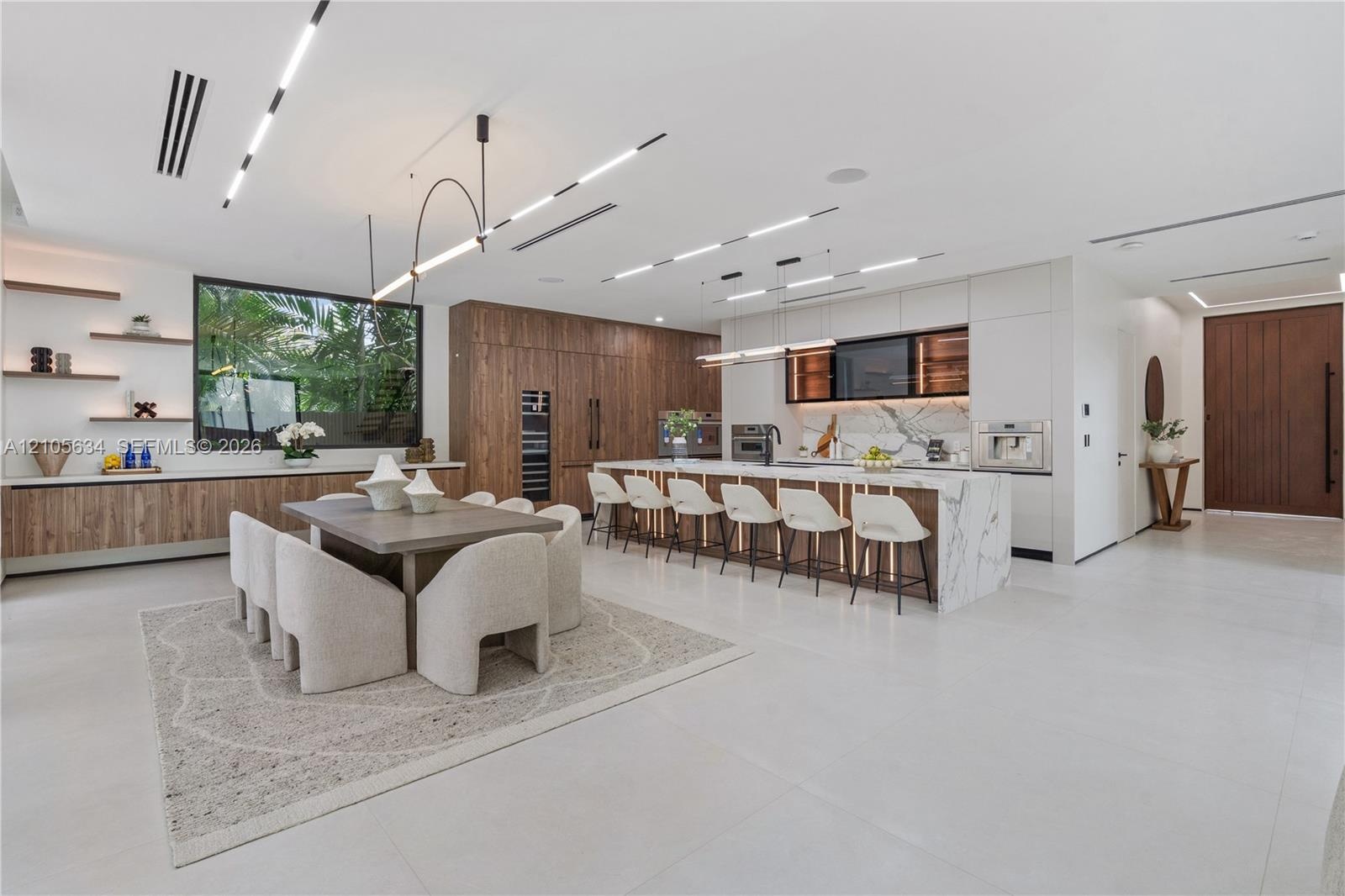 Open-concept kitchen featuring a waterfall-edge stone island, built-in panel-ready appliances, wood-finish cabinetry, linear recessed ceiling lighting