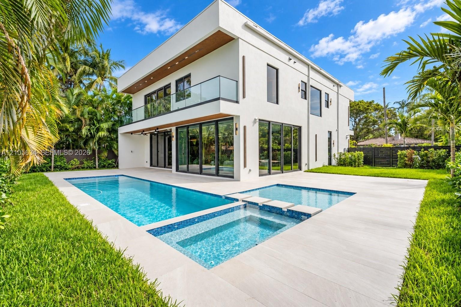 Modern two-story architectural exterior featuring smooth stucco finishes, floor-to-ceiling glass panel doors, a second-level glass-railed balcony, and