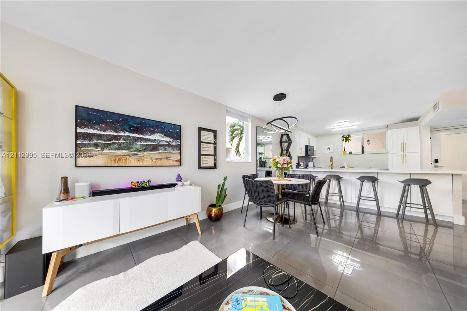 Open-concept interior featuring large-format tile flooring, recessed lighting, a modern multi-ring chandelier, and a kitchen island with integrated se