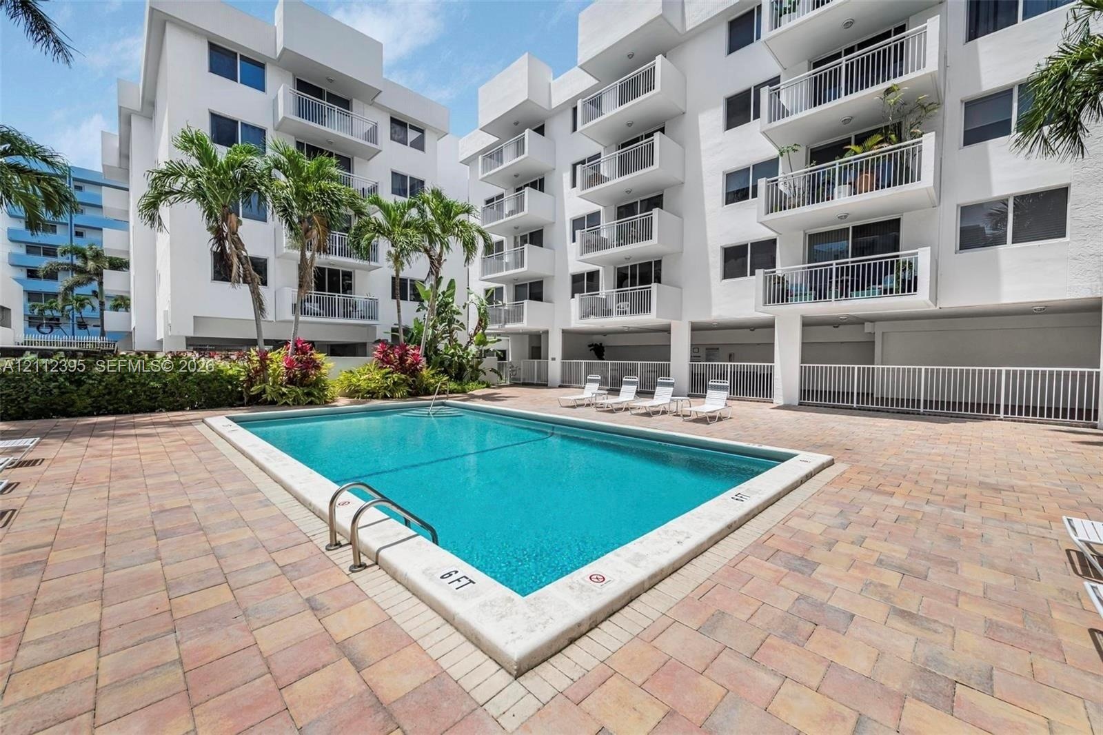 Outdoor swimming pool featuring a concrete deck and paver patio with perimeter fencing and tropical landscaping