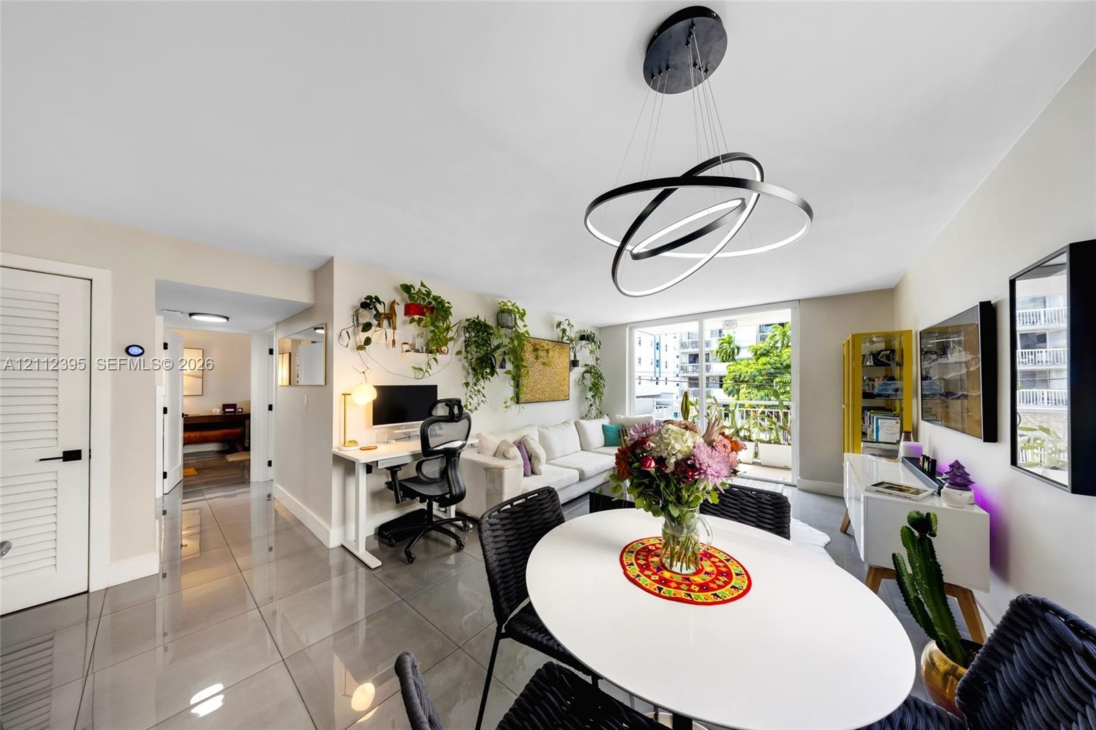 Living area featuring polished large-format floor tiles, contemporary multi-ring circular pendant lighting, and glass sliding doors providing external