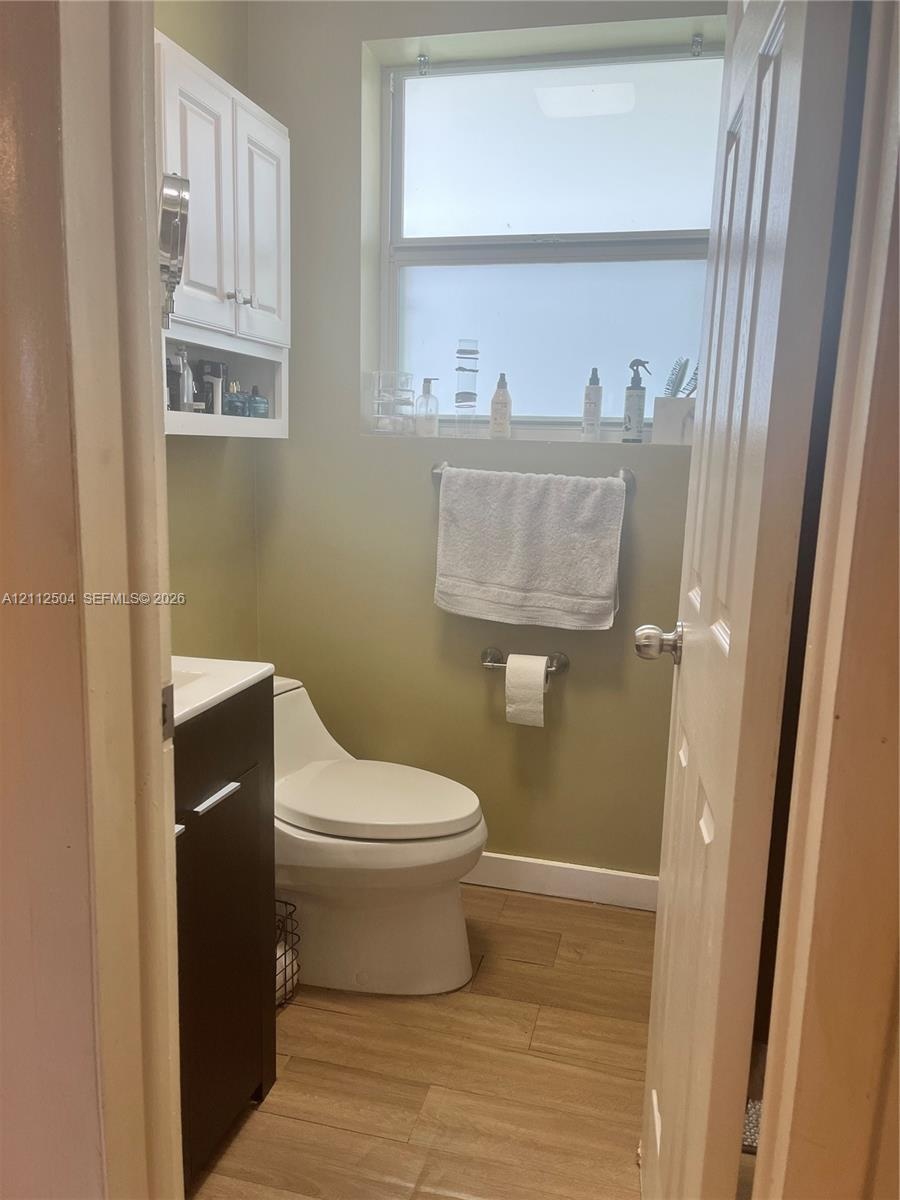 Restroom featuring wood-finish flooring, a contemporary dark-finish vanity, a white high-profile toilet, white built-in wall cabinetry, and an opaque 