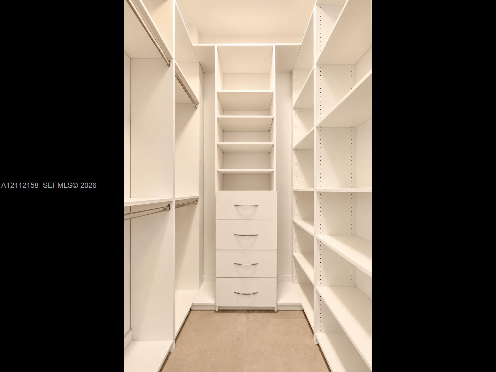 Organized walk-in closet with custom white built-ins, hanging rods, adjustable shelving, and a built-in four-drawer dresser