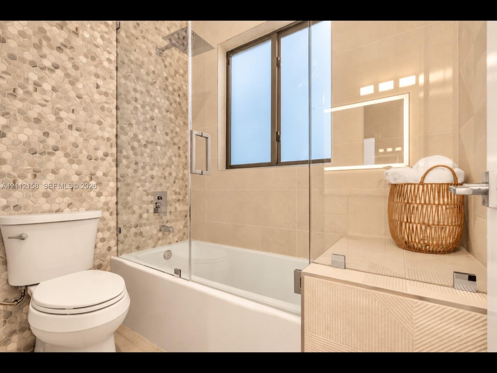 Contemporary bathroom with a glass-enclosed shower, honeycomb tile feature wall, built-in tub, and illuminated vanity mirror