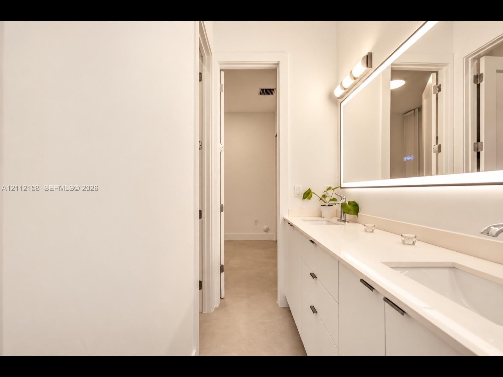 Elegant dual-sink vanity with stone countertop, sleek cabinetry, LED-backlit mirror, and brushed metal hardware