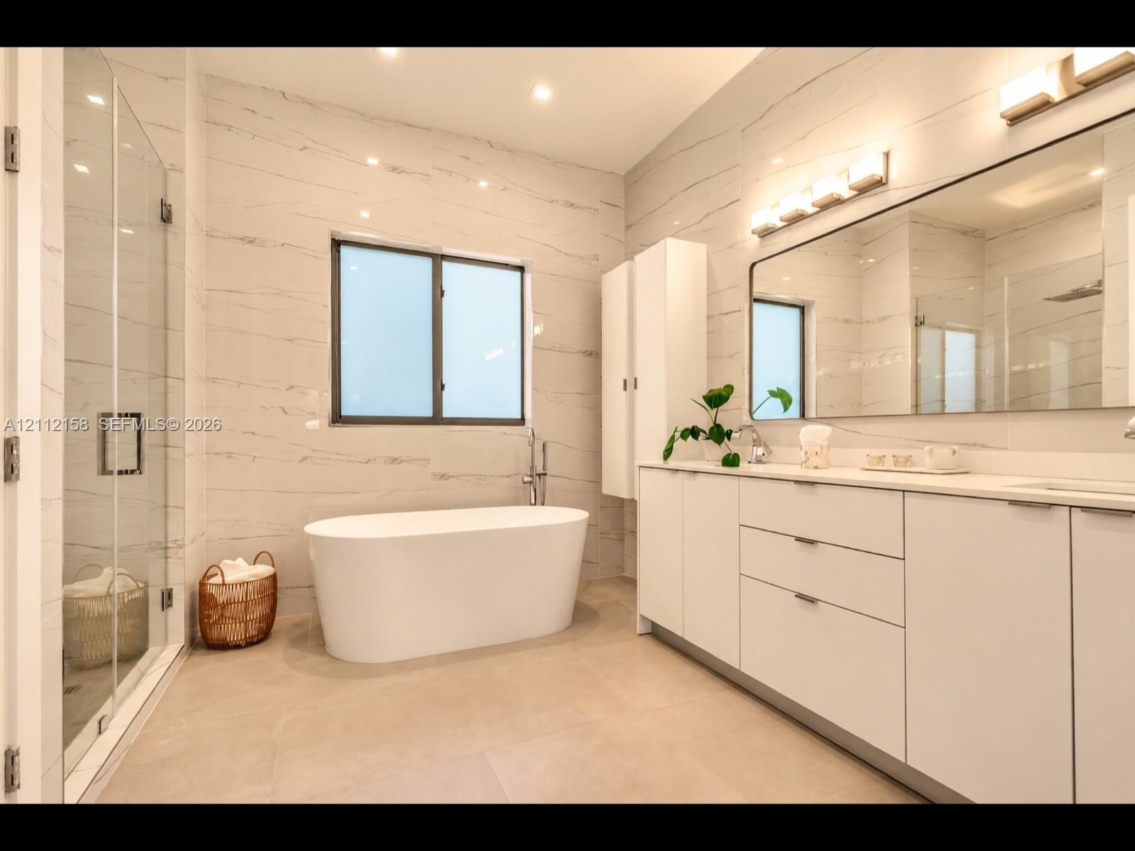 Spa-inspired primary bath with a freestanding soaking tub, glass walk-in shower, double vanity, and full-width illuminated mirror