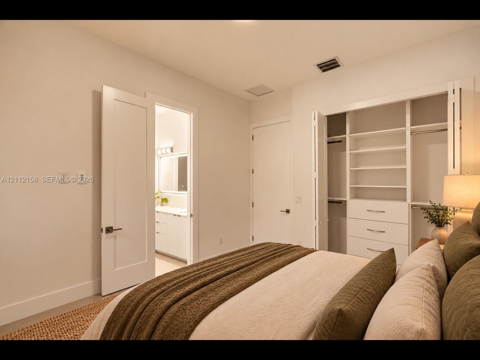 Comfortable bedroom with neutral walls, and a closet with built-in shelving and drawers