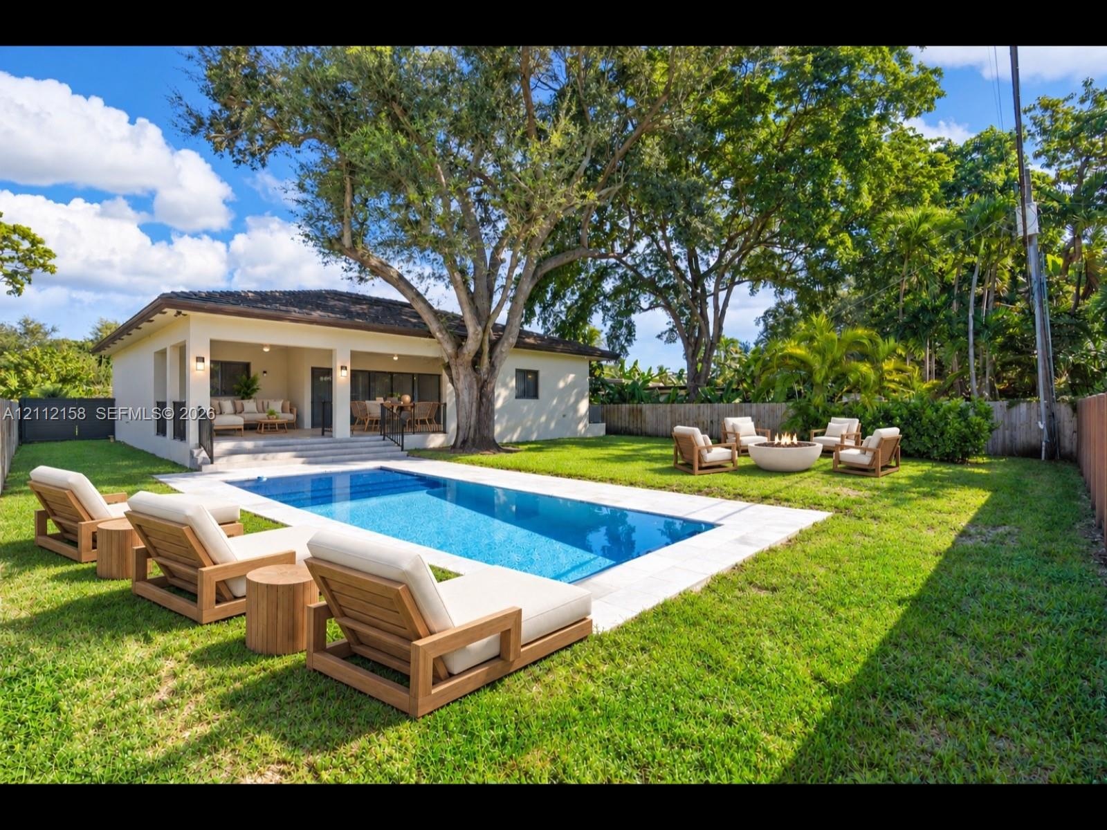 Resort-style backyard with an in-ground pool, stone paver deck, covered patio, and mature trees for natural shade and privacy