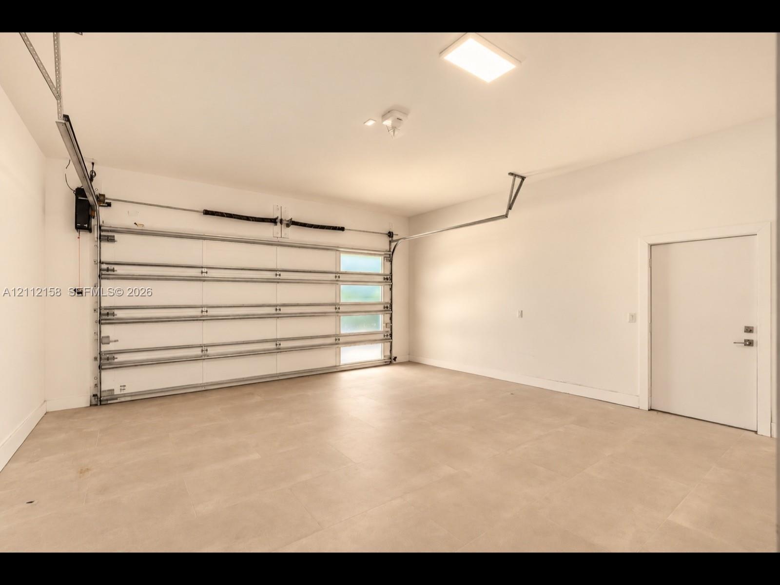 Finished garage with clean tile flooring, bright white walls, frosted-glass garage door for natural light, and direct interior access